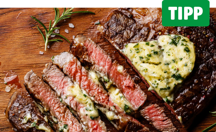 Ein aufgeschnittenes medium-rare Steak liegt auf einem Holzbrett. Die Fleischscheiben sind mit geschmolzener Kräuterbutter überzogen. Auf dem ganzen Stück liegt ein großes Stück Kräuterbutter in Herzform. Oben rechts steht in weißer Schrift auf grünem Grund: Tipp
