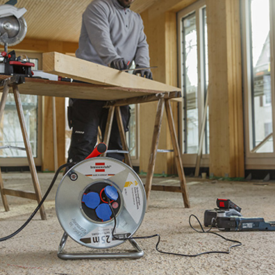 Ein Mann arbeitet im Hintergund an Holz und im Hintergrund sieht man eine Kabeltrommel von Brennenstuhl