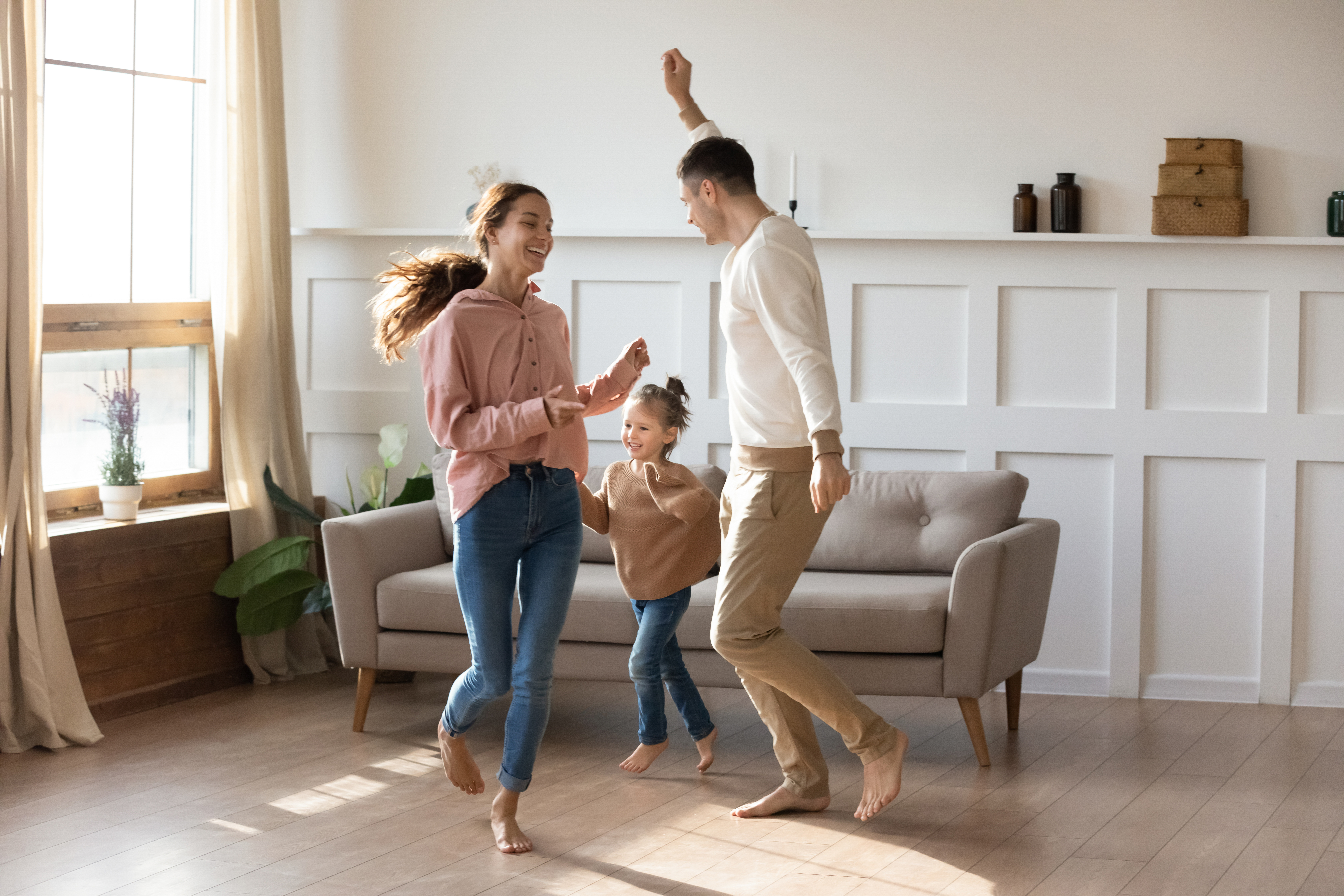 Vater, Mutter und Tochter tanzen in einem gut beleuchtetem Wohnzimmer