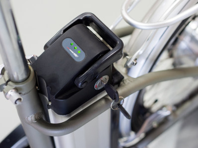 Ein E-Bike-Akku mit Ladeanzeige und eingestecktem Schlüssel ist am Rahmen eines Fahrrads befestigt. Die LED-Leuchten signalisieren den aktuellen Ladestand des Akkus