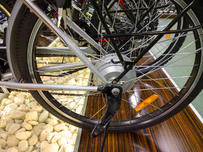 Ein E-Bike steht in einem Ausstellungsraum auf einem Boden aus Holzoptik mit weißen Ziersteinen. Im Fokus steht das Hinterrad mit integriertem Nabenmotor und Ständer