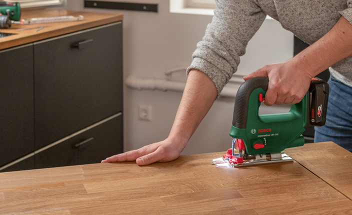 Jemand bohrt mit einer Säge in einen Tisch