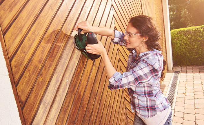 Eine Frau schleift ein Garagentor mit einer Bosch Schleifmaschine