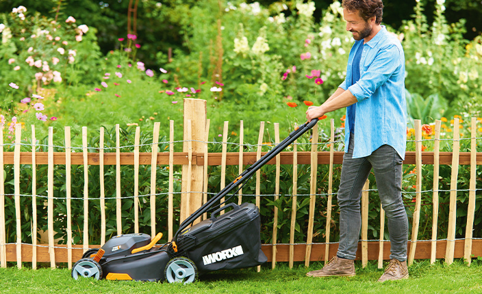 Ein Mann mäht Rasen an einem Zaun entlang