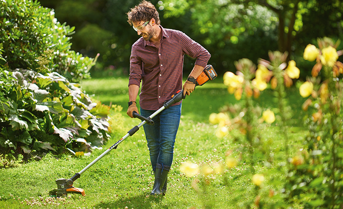 Ein Mann trimmt den Rasen in einem Garten mit einem Rasentrimmer