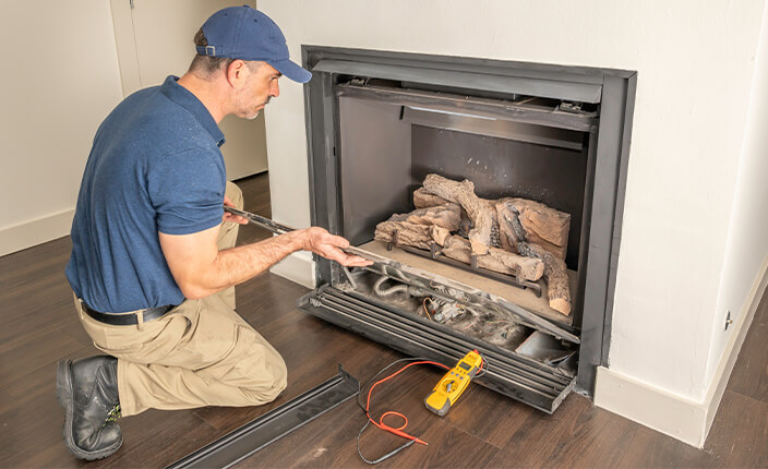 Techniker bei der Wartung eines Gaskamins mit offenem Gehäuse, Werkzeugen und Messgerät auf dem Boden.