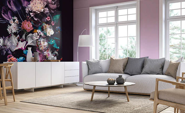 Helles Wohnzimmer mit pastelllila Wänden, großem Sofa und einer eindrucksvollen Akzentwand mit großformatiger, dunkel gehaltener Blumentapete links neben einem weißen Sideboard.