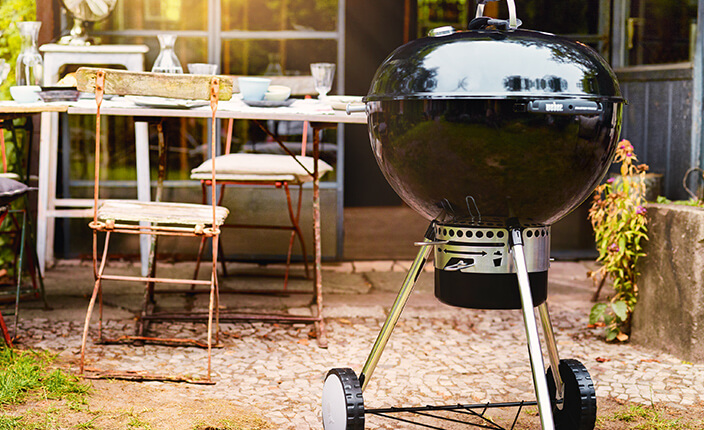 Ein Holzkohlegrill in einem kleinen Garten mit einem Essenstisch im Hintergrund