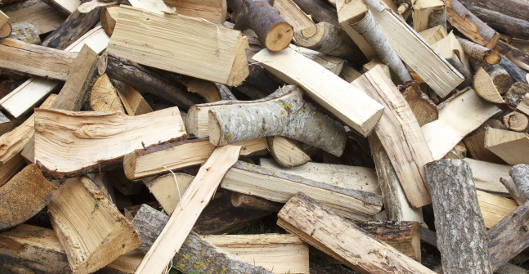 Ein großer Haufen frisch gespaltenes Brennholz mit unterschiedlichen Holzarten, Längen und Rindenanteilen liegt unsortiert aufeinander.