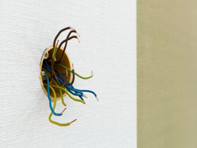 Geöffnete Unterputzdose in einer Wand, aus der mehrere Elektrokabel ragen