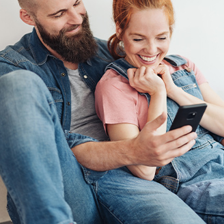 Eine Frau und ein Mann sitzen mit dem Rücken an einer Wand und schauen gemeinsam auf ein Tablet