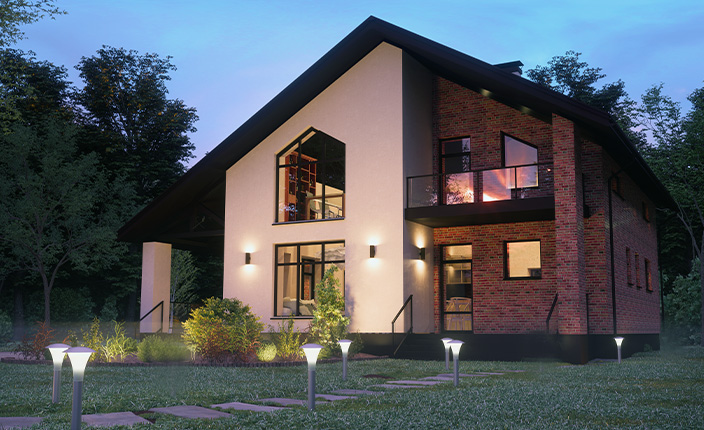 Ein Einfamilienhaus mit auffälliger Außenbeleuchtung und Weglichtern, umgeben von Rasen, Büschen und Bäumen in der Abenddämmerung.