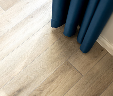 Heller Holzfußboden mit blauem Vorhang und einem Ausschnitt eines beigen Teppichs.