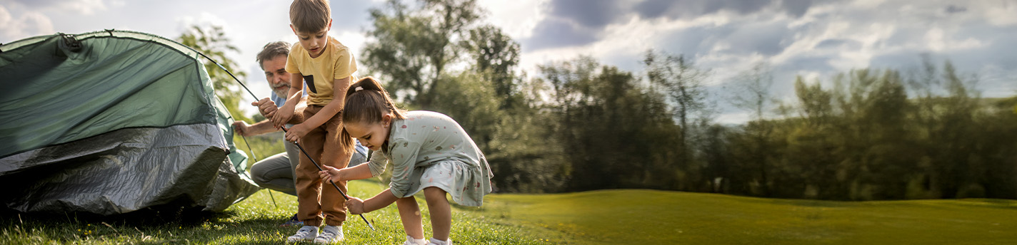 Ein Vater baut mit seinen zwei Töchtern ein Zelt auf.