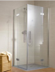 Die minimalistische Kabine einer Eckdusche mit mattiertem Glas und verchromten Beschlägen ist in einem hell gefliesten Badezimmer installiert. Neben der Dusche steht ein Wäschekorb aus Holz