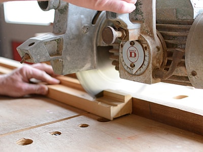 Ein Stück Holz wird mit einer Kreissäge auf einer Werkbank zugeschnitten. Eine Hand führt das Holz, die rotierende Säge ist im Einsatz.