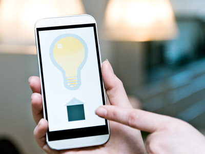 Eine Person steuert über eine App auf dem Smartphone das Licht in einem Smart-Home-System