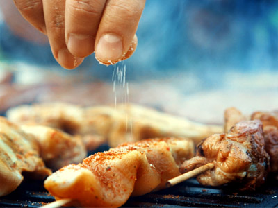 Grillspieße auf einem Grillrost werden per Hand gesalzen