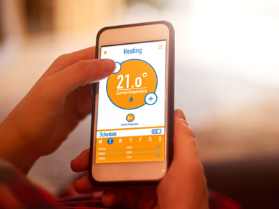 Eine Person nutzt eine Heizungssteuerungs-App auf dem Smartphone zur Einstellung der Raumtemperatur und des Zeitplans