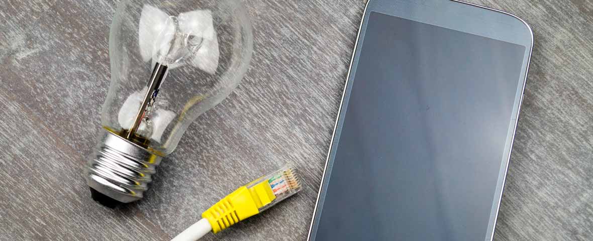 Eine Glühbirne, ein gelbes Netzwerkkabel und ein Smartphone liegen nebeneinander auf einem Holztisch