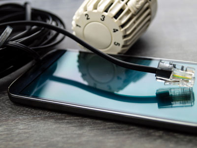 Ein klassischer Heizkörperregler, ein Netzwerkkabel und ein Smartphone liegen auf einem Tisch