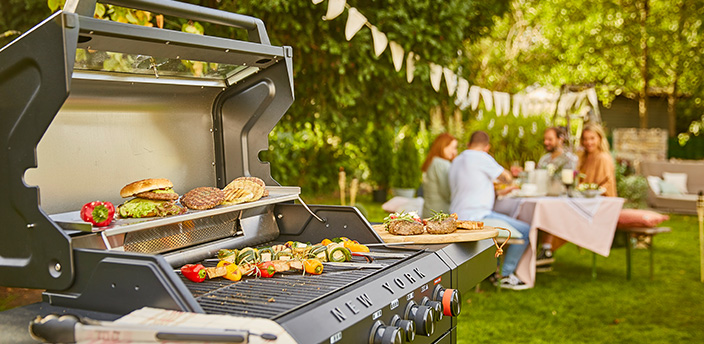 Eine Familie grillt in ihrem Garten. Auf dem Grill befindet sich reichlich Essen